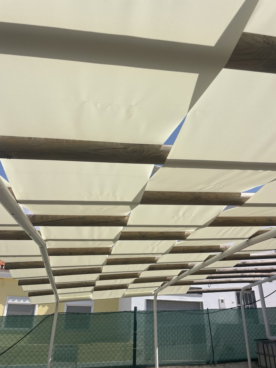 Close-up underside of pergola with cream fabric woven between wooden beams, Algarve
