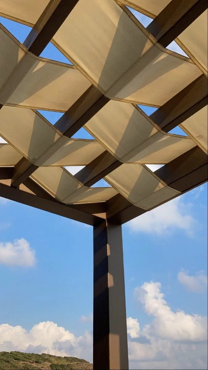 View looking up at woven fabric pergola shade canopy against blue sky, Algarve