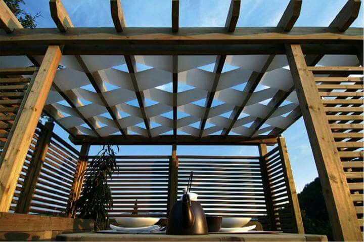 Wooden pergola with fabric shade panels between beams, view from below against blue sky