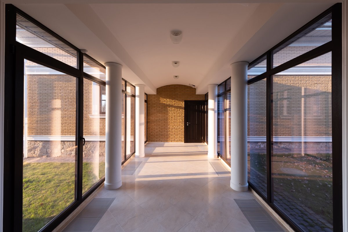 Glass corridor with tinted windows and white columns, sunlit interior