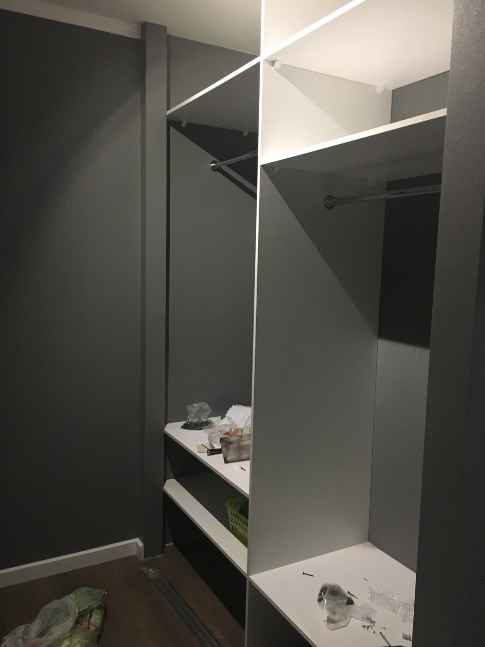 Built-in wardrobe with hanging rails and shelves being installed in dark-walled room, Algarve